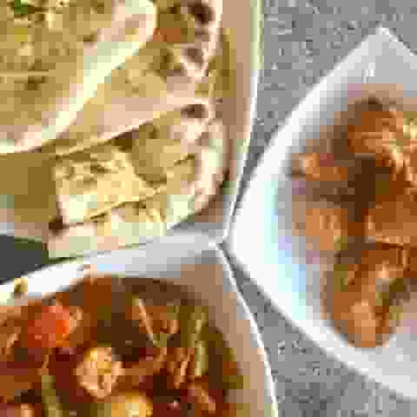 Three dishes of Indian food, including naan bread, a curry, and another savory dish.