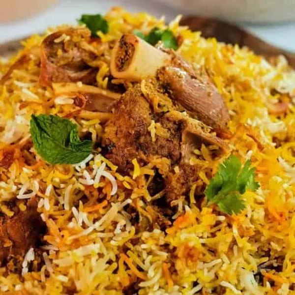 Close-up of lamb biryani with tender meat, bone, and fresh mint leaves on colorful rice.