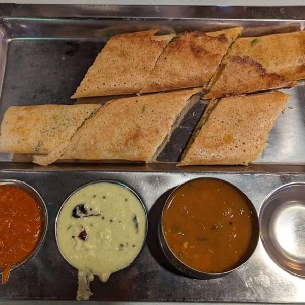 Crispy dosas cut into pieces, served with three different chutneys on a metal tray.