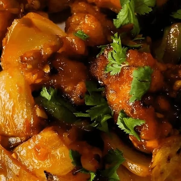 Close-up of chili paneer with bell peppers and cilantro, coated in a glossy, dark orange sauce.